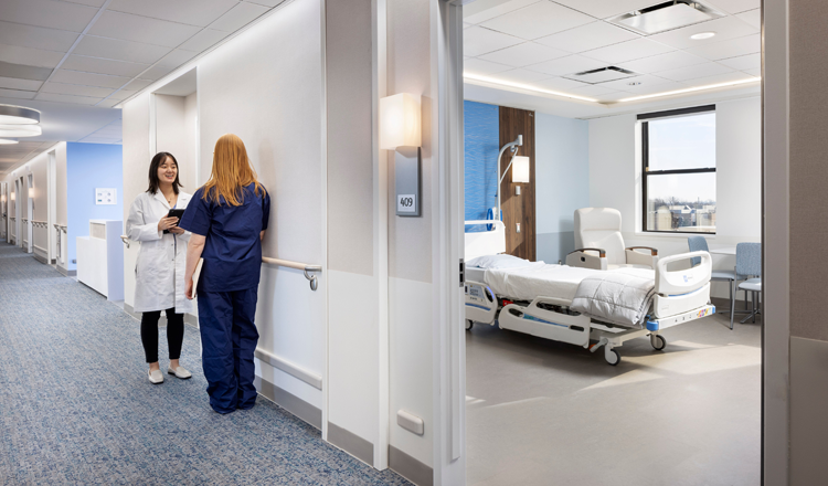 Hospital ward with two healthcare workers. Hospital bed in the background.