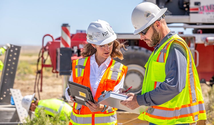 people on construction site looking comparing notes with tablet and clipboard