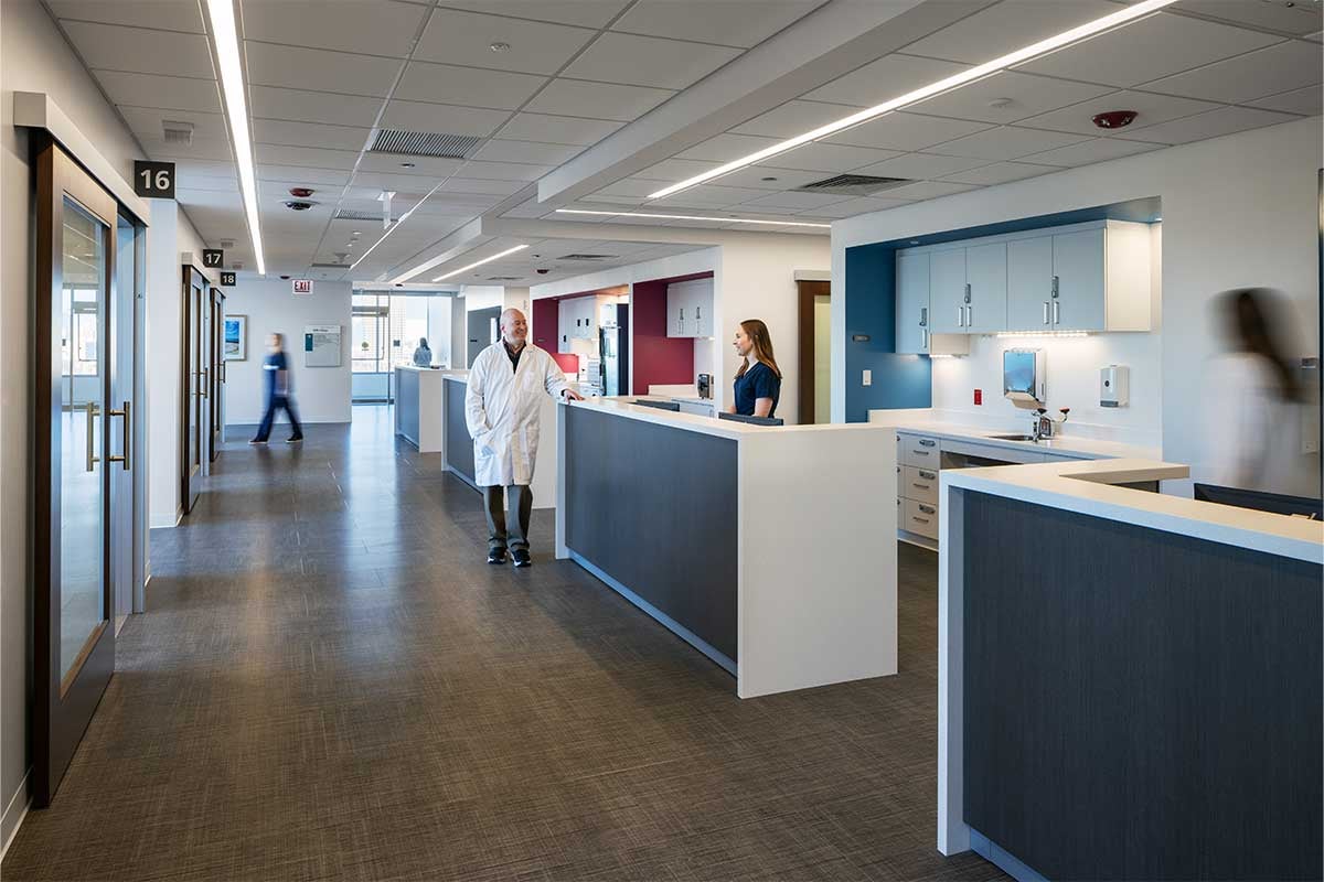 Interior shot of hospital corridor with reception areas. There are medical professionals walking throughout the shot