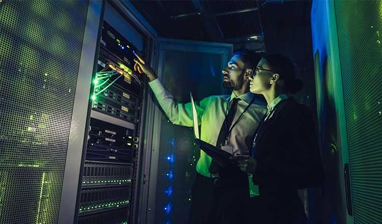 A man and woman in a data center, engaging with a touchscreen display.