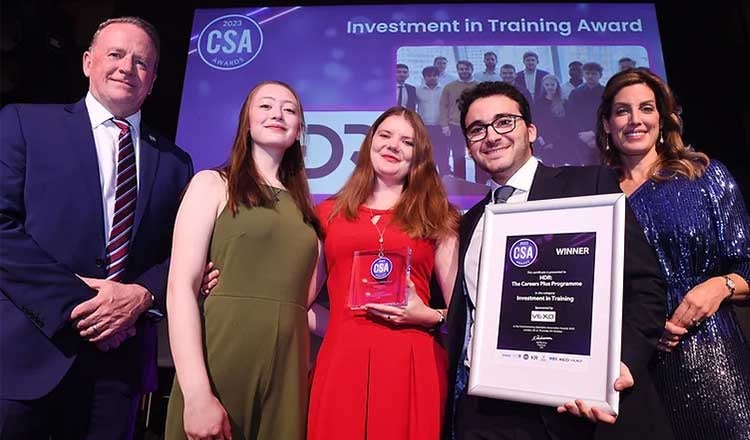 Four people posing on stage with an award certificate. 