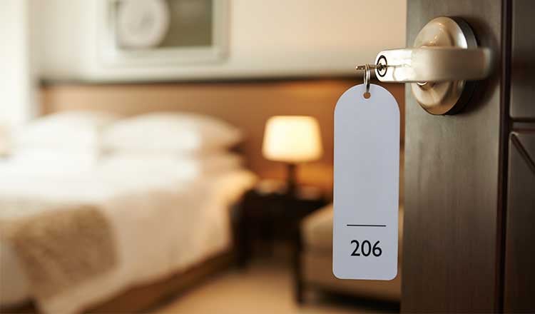 Open hotel room door with handle in foreground and hotel bed in the background.