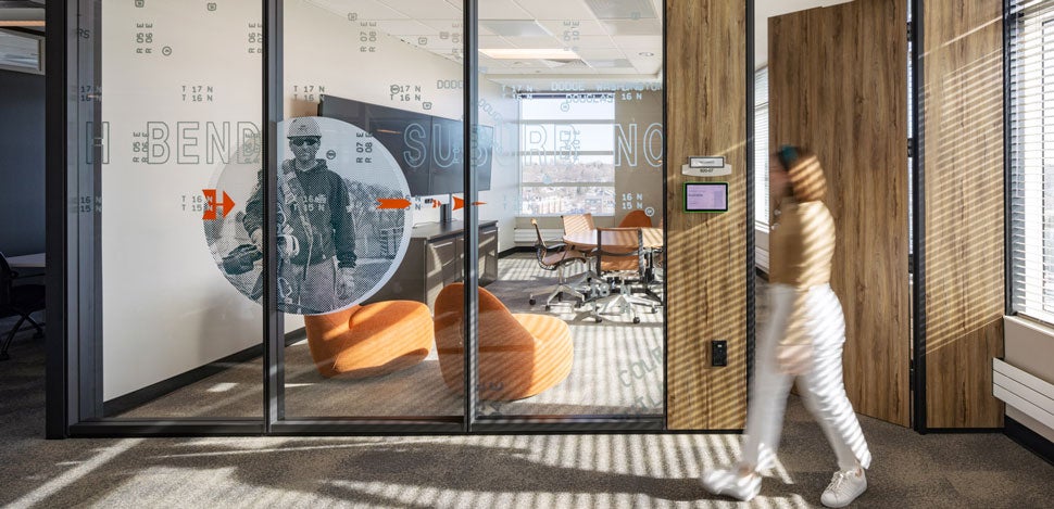 Person walking by a meeting room with floor-to-ceiling glass windows in an office