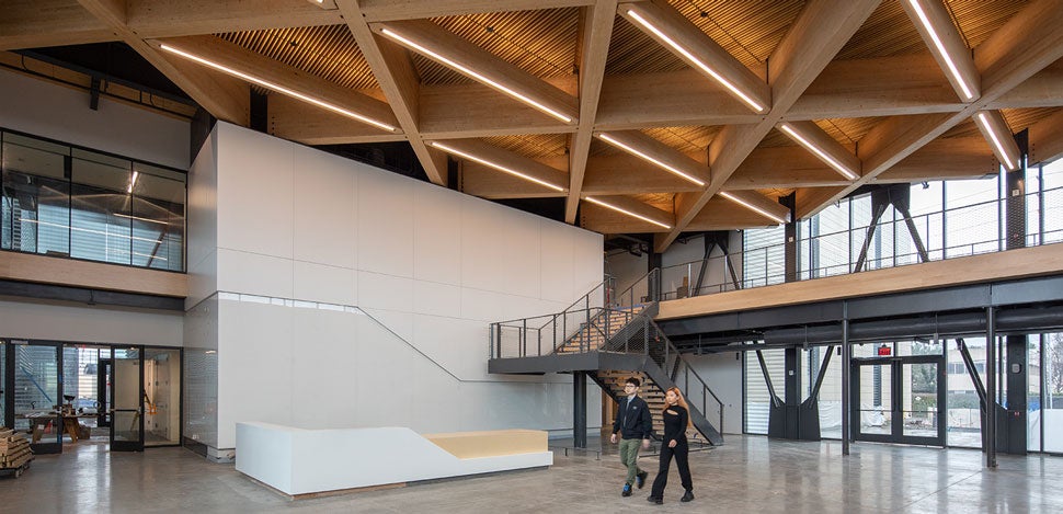 The lobby of a facility with an illuminated, timber ceiling and two people walking through