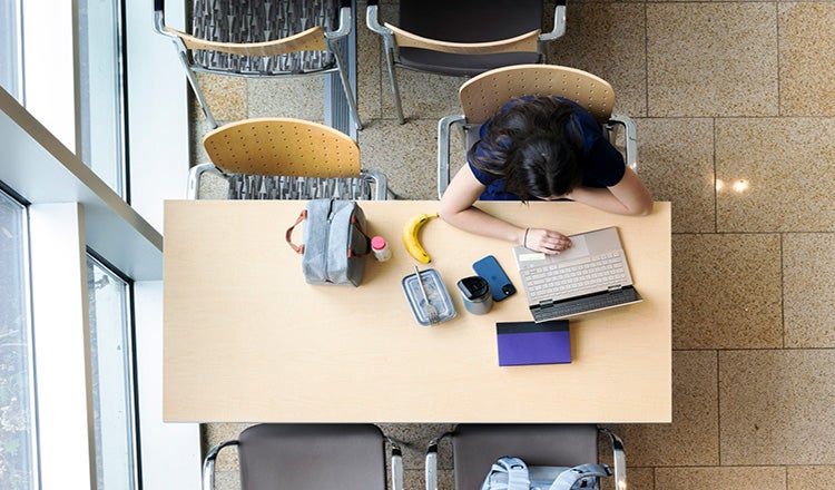 Photo taken from above of a student doing work on a laptop at a table in a communal area in a university