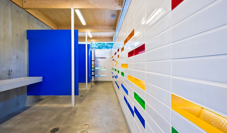 Public restroom with blue dividers, colorful wall, mass timber ceiling