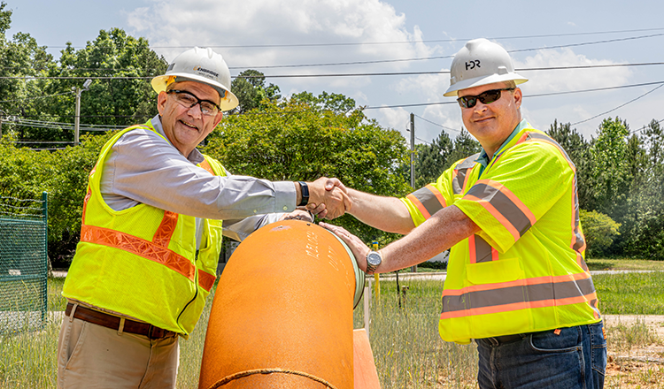 Two people shaking hands near a pipeline