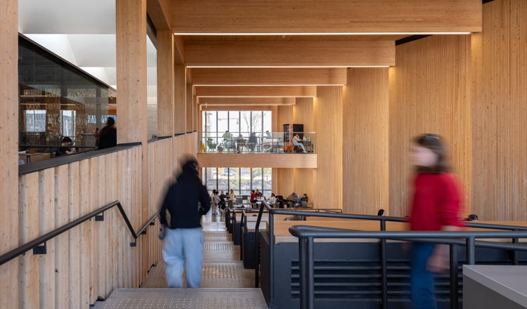 Study atrium in a university building with wood interiors, students passing by