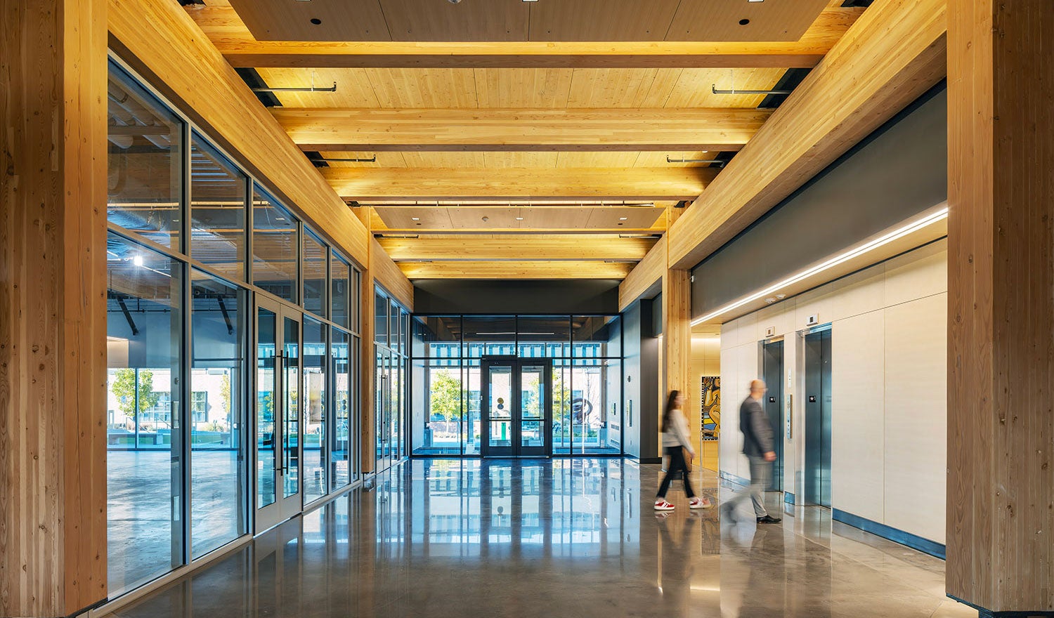A lobby of a building with mass timber interiors and recessed lighting and people walking