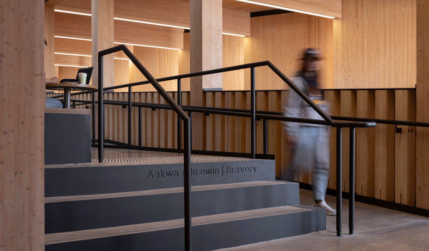 A student walking up to a staircase in a university auditorium with wood interiors
