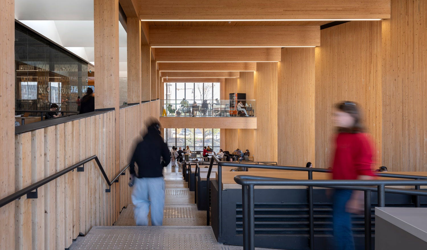 Students in a university auditorium with wood interiors, tables, and a main staircase